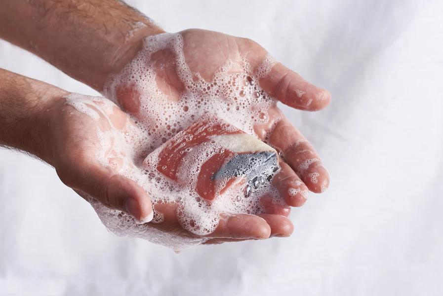 Close-up of a hand being washed with soap, covered in thick, foamy bubbles.