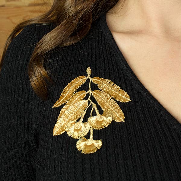 A person wearing the Botanopia Eucalyptus flowers embroidery brooch on a black V-neck sweater.