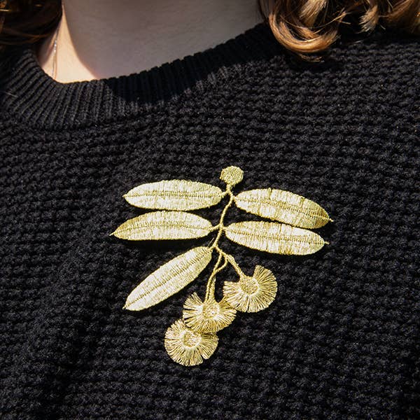 A person wearing the Botanopia Eucalyptus flowers embroidery brooch on a black sweater.