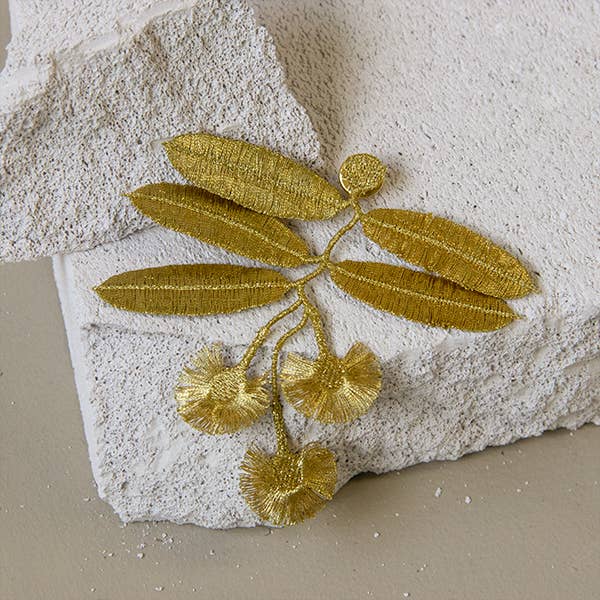 Botanopia Eucalyptus flowers embroidery brooch lying on a rock with a white backdrop.