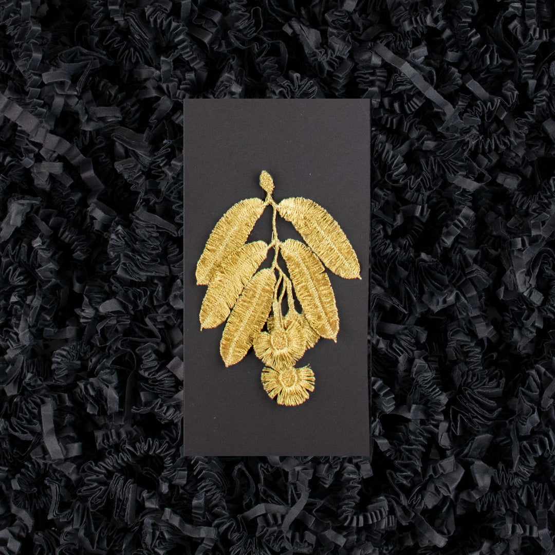 Botanopia Golden Eucalyptus flowers embroidery brooch placed on a black gift box with a black backdrop.