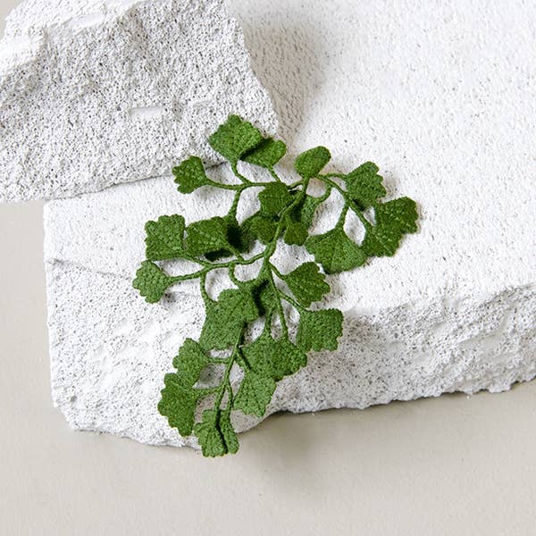 Botanopia Maidenhair fern embroidery brooch lying on a rock with a white backdrop.