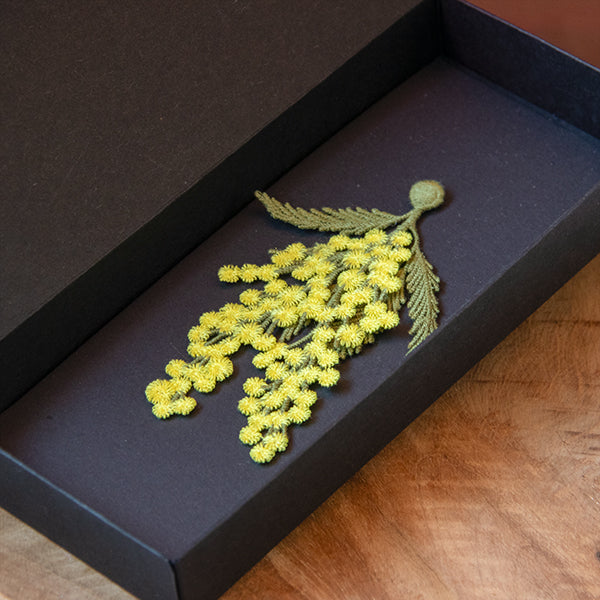 Open black gift box containing the Botanopia mimosa embroidery brooch.