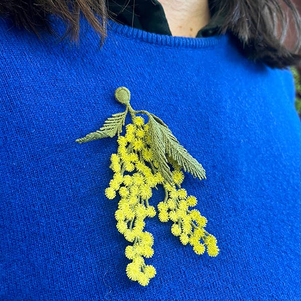 A person wearing the Botanopia mimosa embroidery brooch on a blue cardigan.