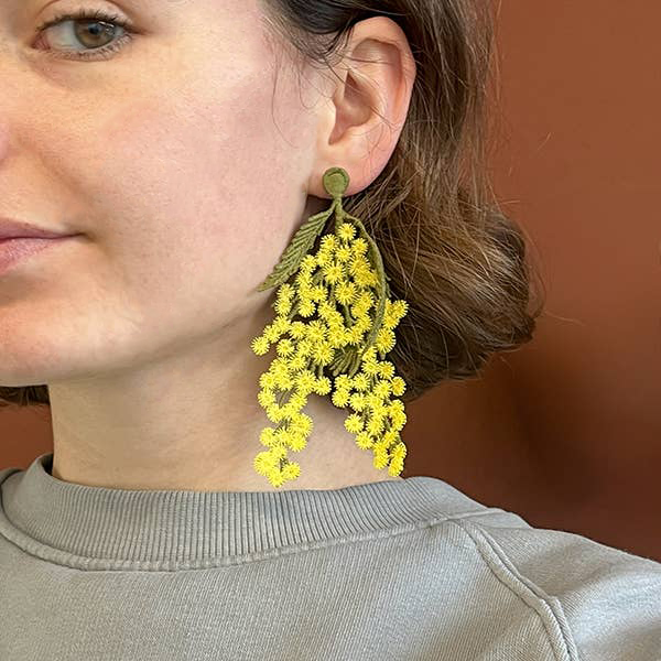 A woman wearing the Botanopia mimosa embroidery brooch as an earring.