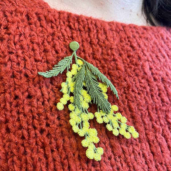 A person wearing the Botanopia mimosa embroidery brooch on a red sweater.