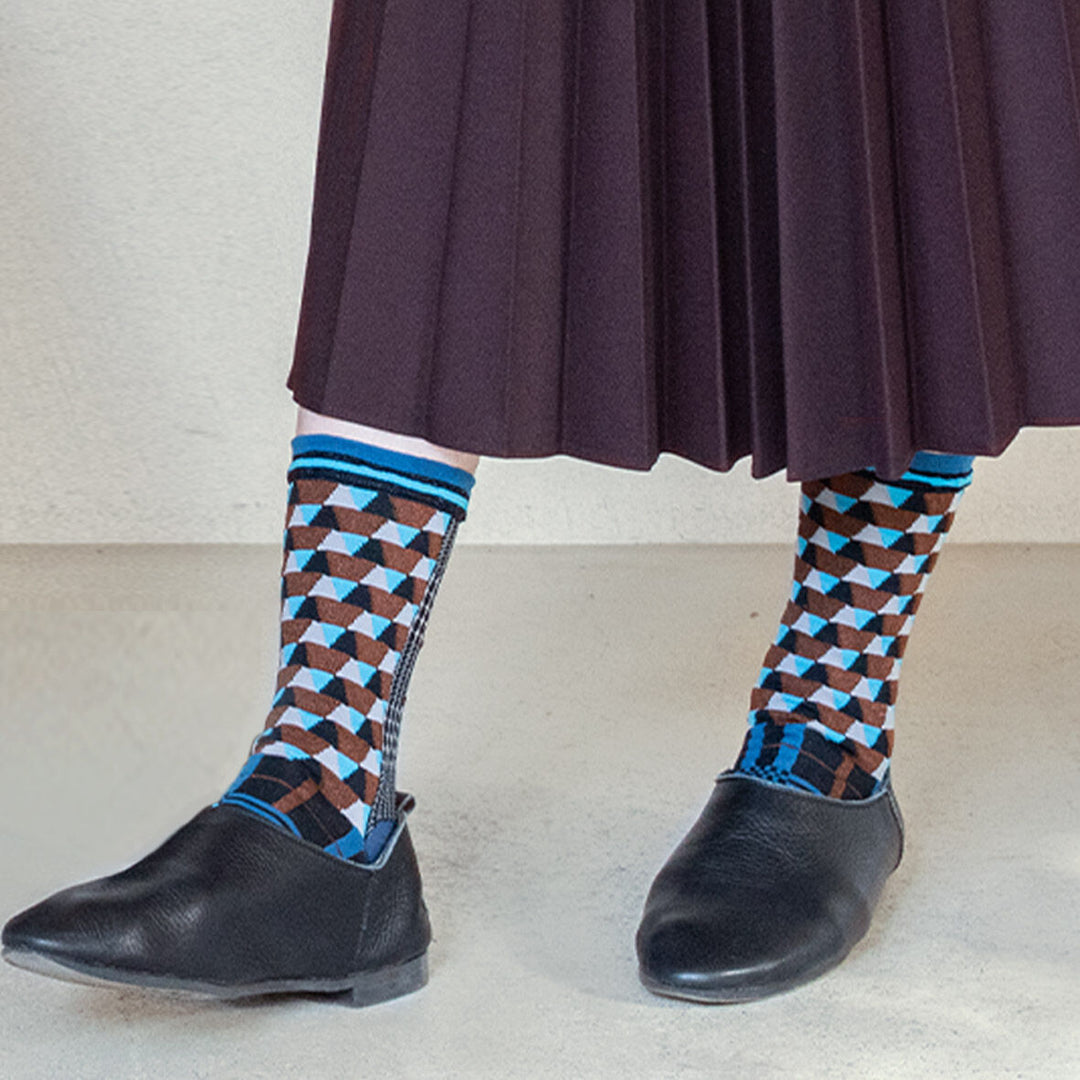 A model wearing Antique Patch Blue socks paired with a flowing brown long dress, showcasing the unique geometric patterns of the socks.