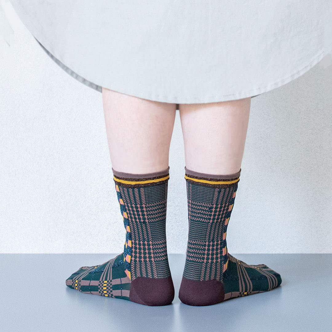 A model wearing Antique Patch socks in dark green, styled with a beige dress, highlighting the unique geometric patterns of the socks.