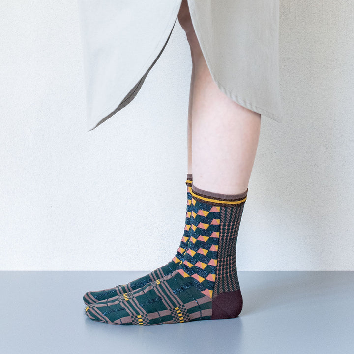 A model wearing Antique Patch socks in dark green, styled with a beige dress, highlighting the unique geometric patterns of the socks.