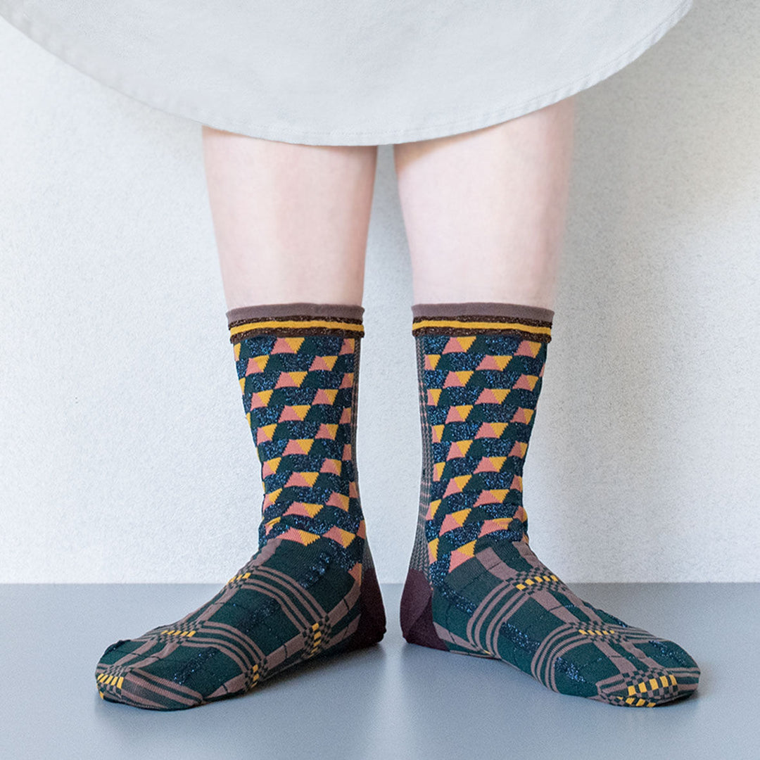 A model wearing Antique Patch socks in dark green, styled with a beige dress, highlighting the unique geometric patterns of the socks.