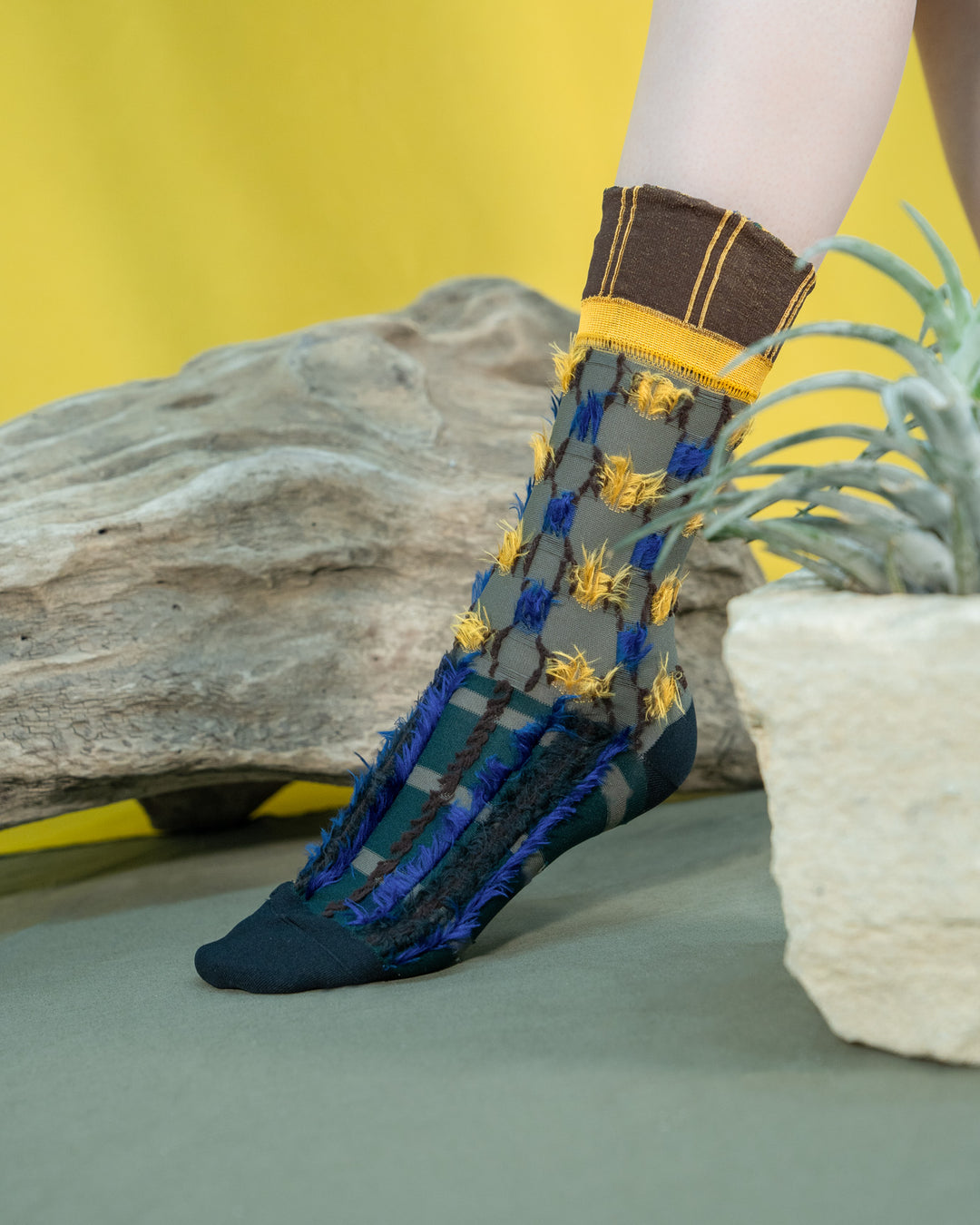 A model wearing Atelier Textiles socks in blue, yellow, and grey, made in Japan, showcasing their unique patterns and versatility against a stylish outfit.