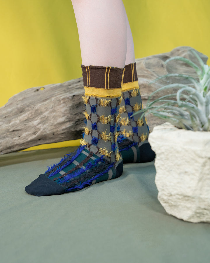 A model wearing Atelier Textiles socks in blue, yellow, and grey, made in Japan, showcasing their unique patterns and versatility against a stylish outfit.