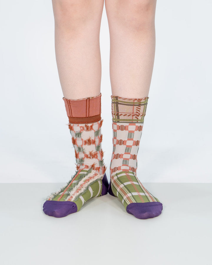 A model wearing Atelier Textiles Pink socks in green, purple, and orange on her legs, made in Japan, showcasing different ways to wear them against a white background.