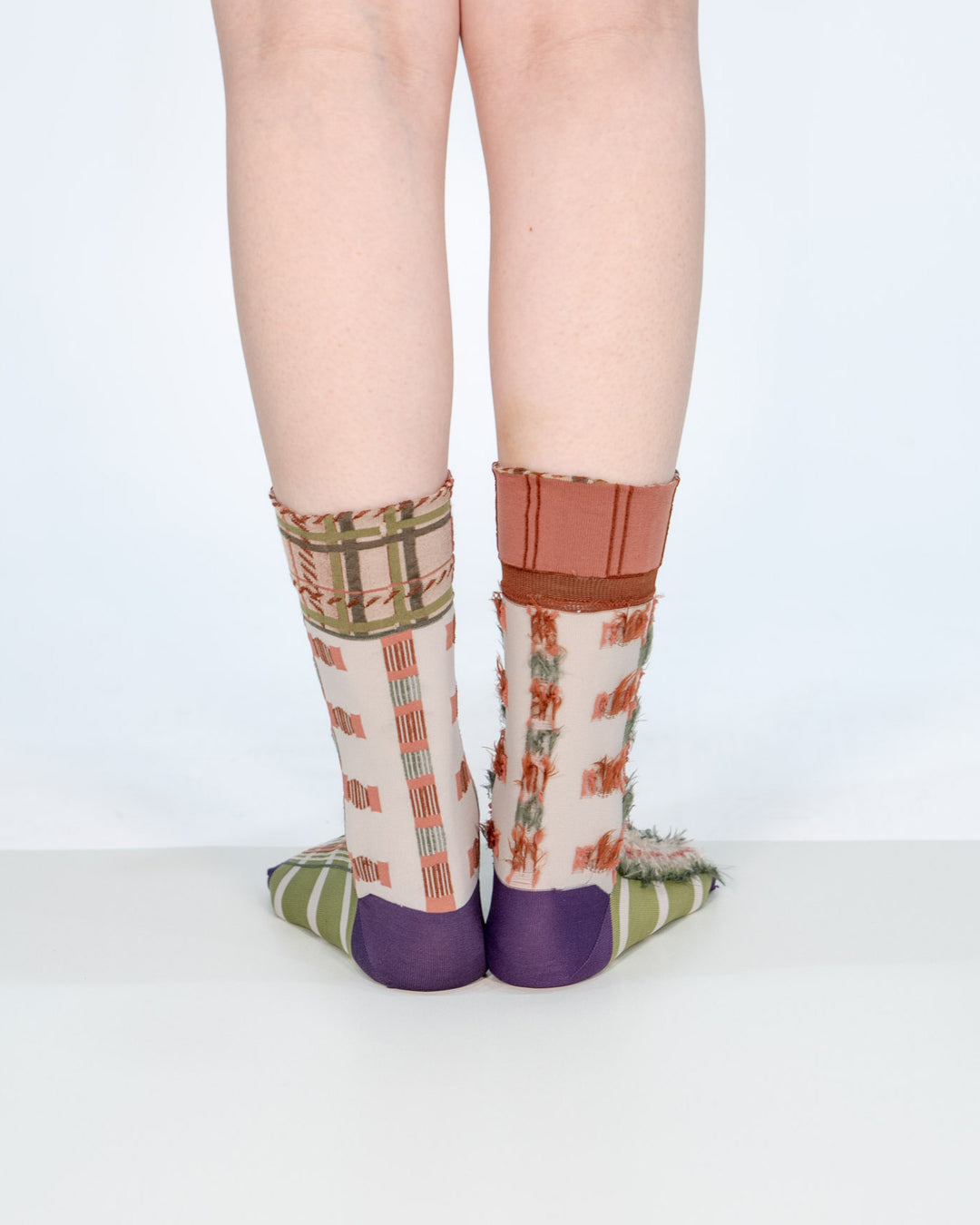 A model wearing Atelier Textiles Pink socks in green, purple, and orange on her legs, made in Japan, showcasing different ways to wear them against a white background.