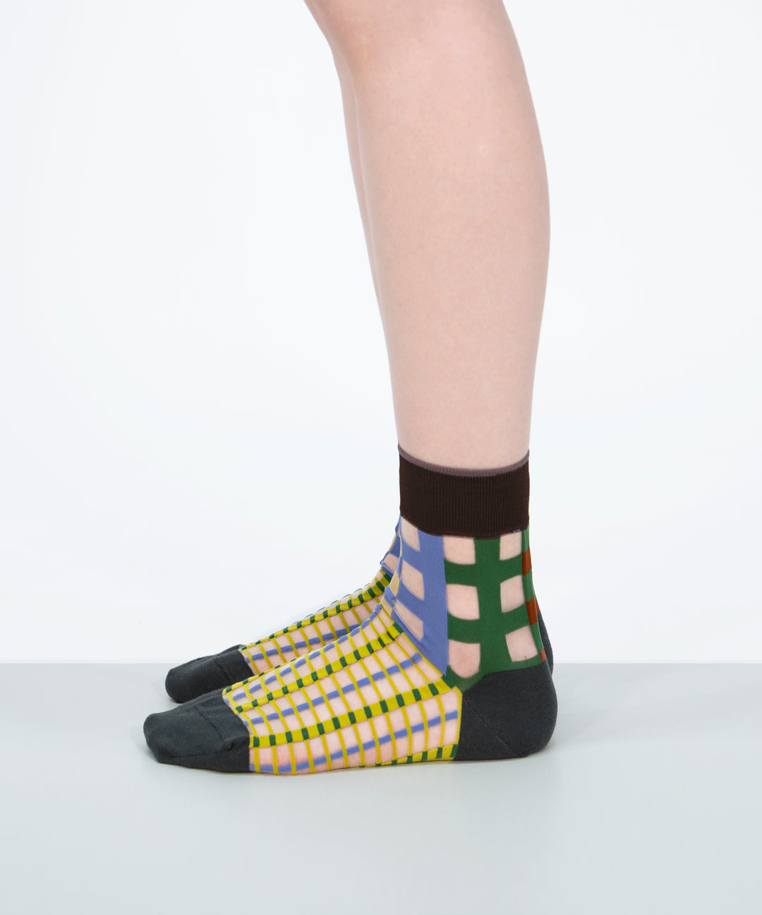 A model wearing COQ Picnic Window Socks in green, made in Japan, showcasing the checked pattern and translucent design on her leg.