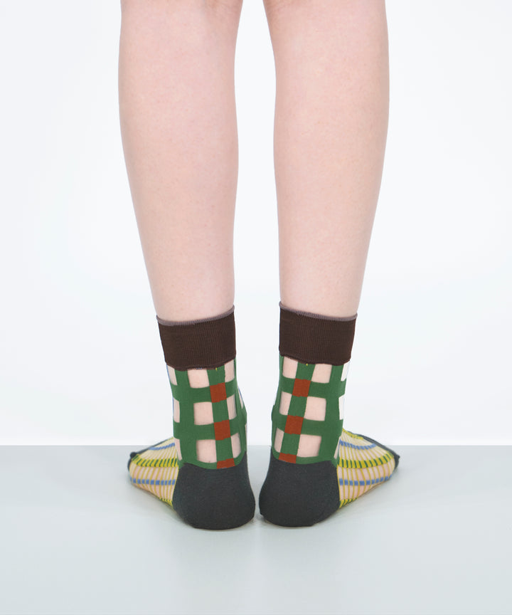 A model wearing COQ Picnic Window Socks in green, made in Japan, showcasing the checked pattern and translucent design on her leg.