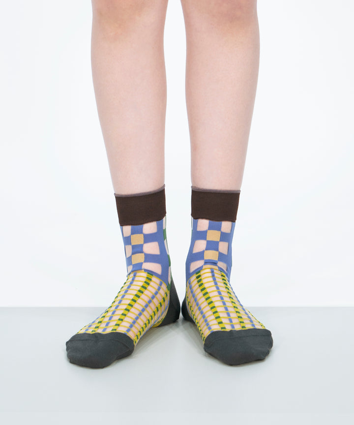 A model wearing COQ Picnic Window Socks in green, made in Japan, showcasing the checked pattern and translucent design on her leg.