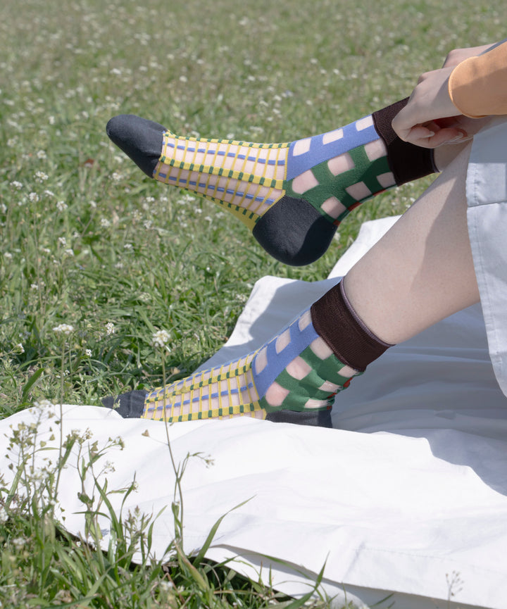 A model wearing COQ Picnic Window Socks in green, made in Japan, enjoying a picnic on a mat, styled with a white dress that complements the socks.