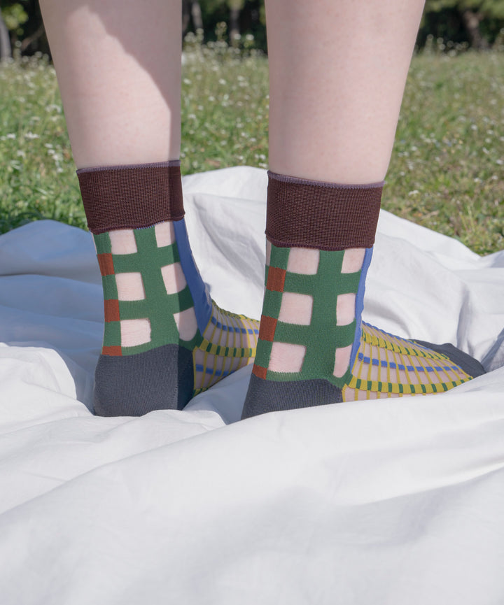 A model wearing COQ Picnic Window Socks in green, made in Japan, enjoying a picnic on a mat, styled with a white dress that complements the socks.