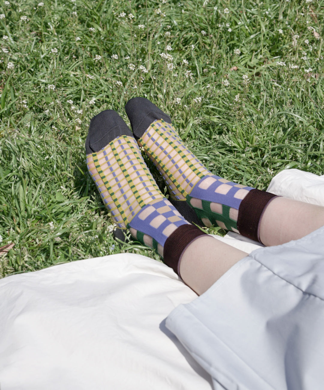 A model wearing COQ Picnic Window Socks in green, made in Japan, enjoying a picnic on a mat, styled with a white dress that complements the socks.