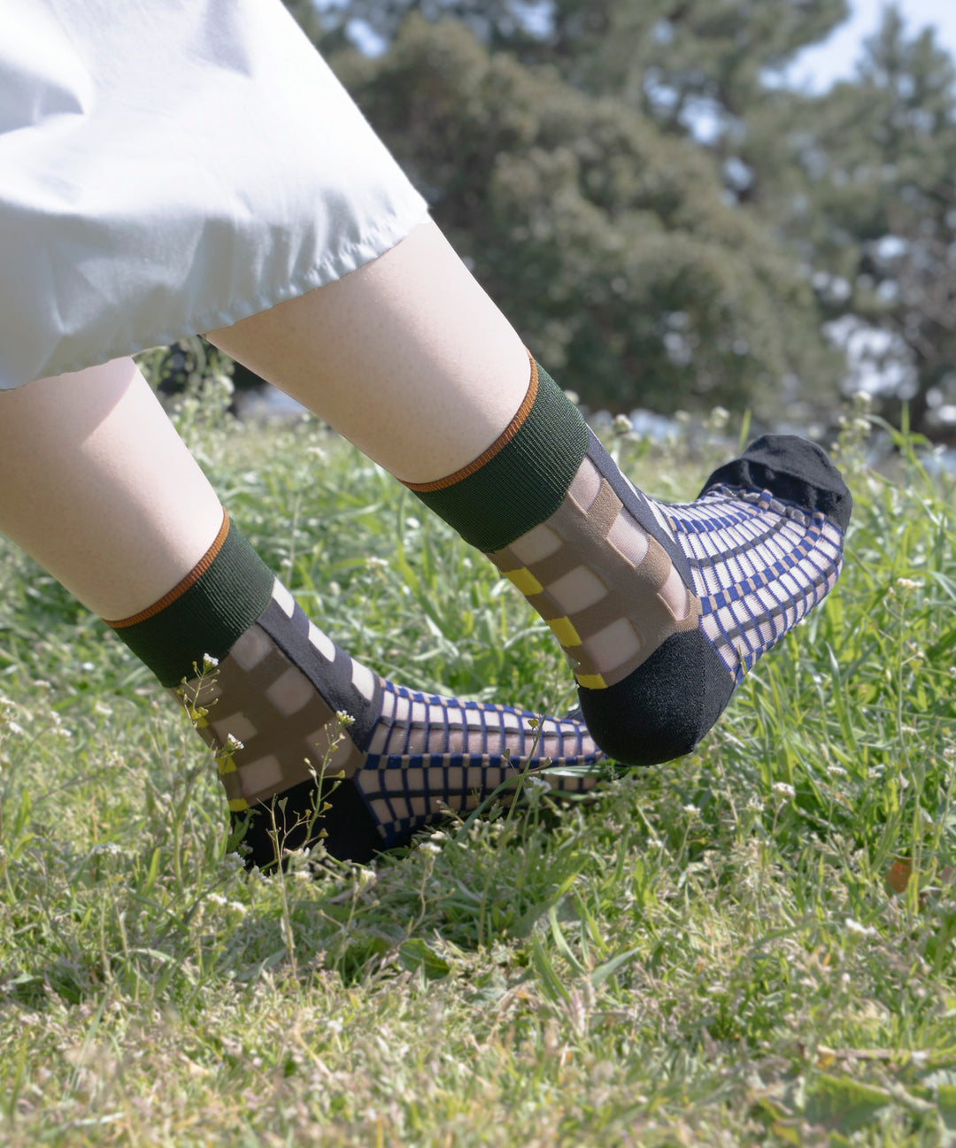 A model wearing COQ Picnic Window Socks in navy, made in Japan, enjoying a picnic on a mat, showcasing the checked pattern and translucent design.