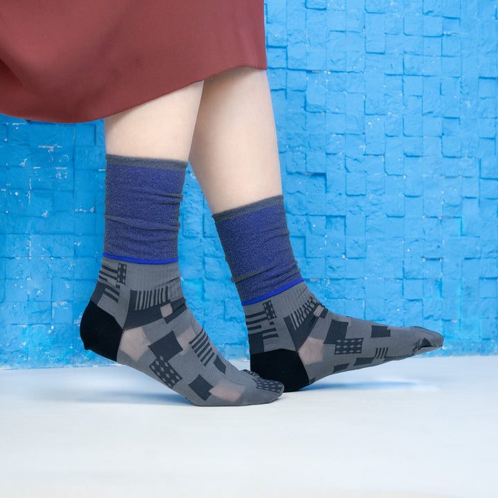 A model wearing COQ Sunlight Block Socks in black, made in Japan, styled with a brown dress, showcasing the unique geometric patterns of the socks.