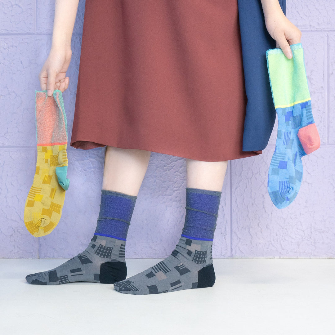 A model wearing COQ Sunlight Block Socks in black, made in Japan, while holding a pair of socks in blue and yellow in her hand.