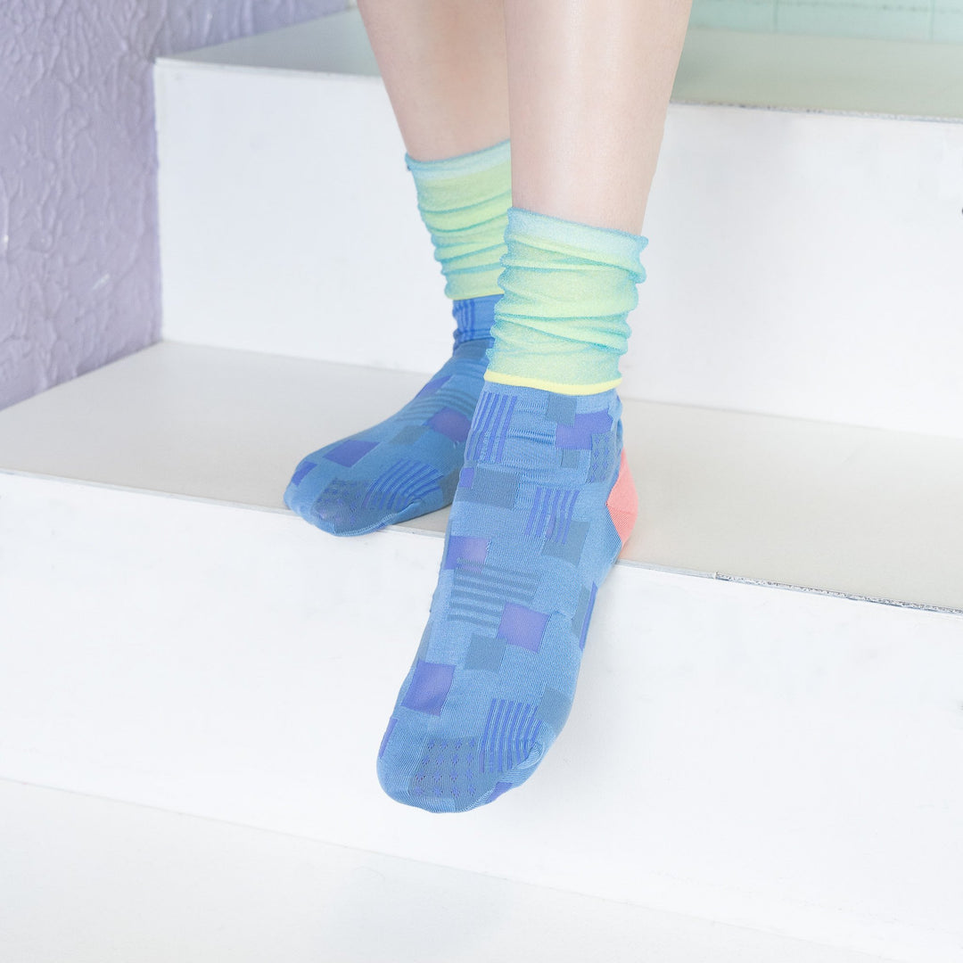 A model wearing COQ Sunlight Block Socks in blue, made in Japan, styled with a brown dress, showcasing the unique geometric patterns of the socks.