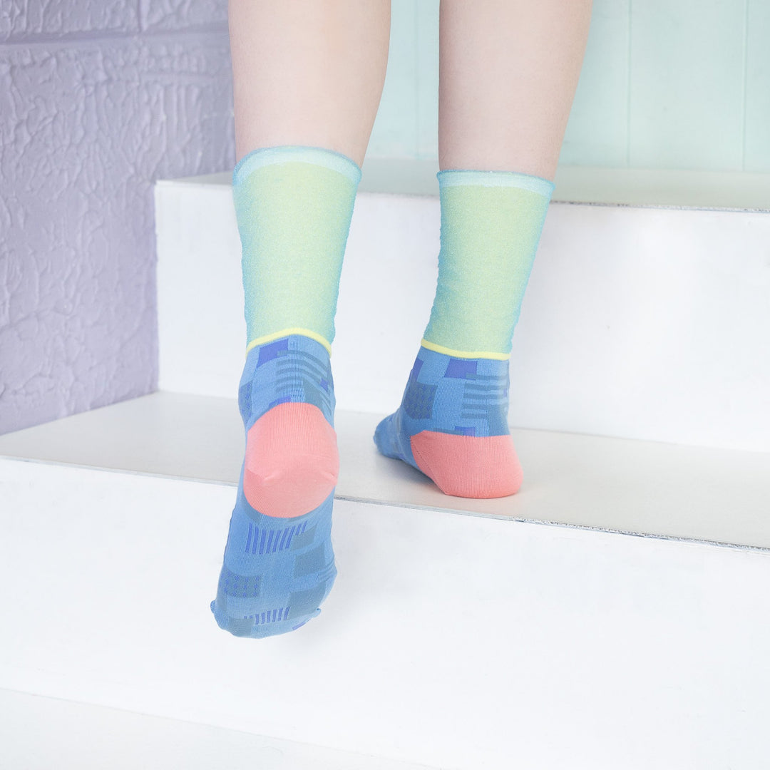 A model wearing COQ Sunlight Block Socks in blue, made in Japan, styled with a brown dress, showcasing the unique geometric patterns of the socks.