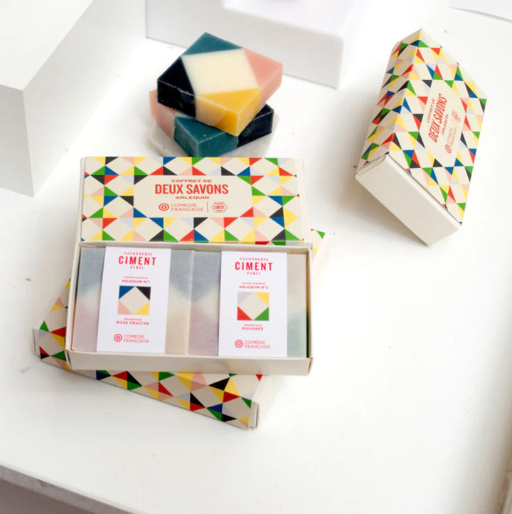 Opened organic Ciment Arlequin soap gift box on a desk with two unwrapped colorful soaps beside it.