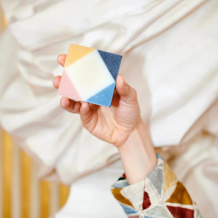 A hand holding colorful organic Ciment Arlequin Poudrée soap.