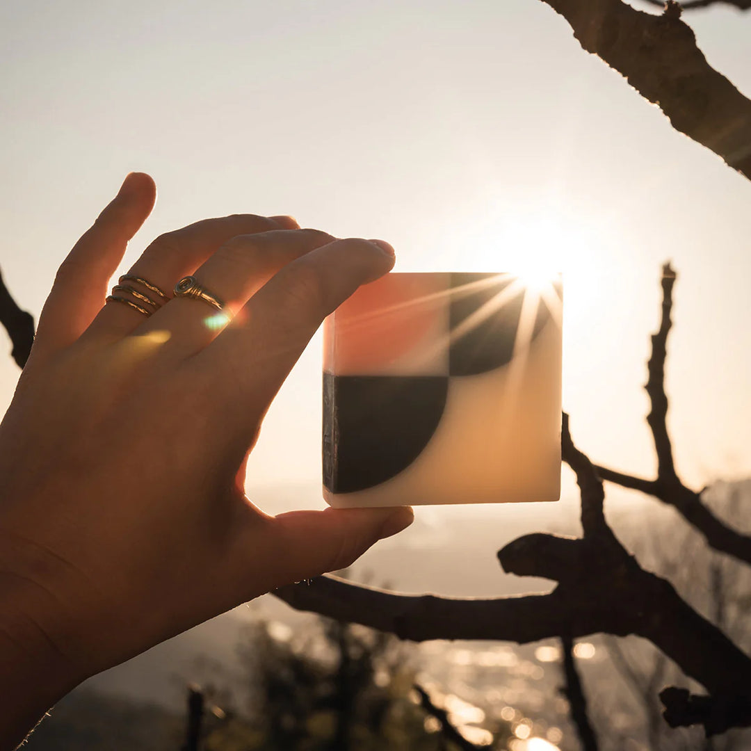 An organic Ciment Kimono Fleur de Cerisier soap held by a hand, with sunlight shining on it.