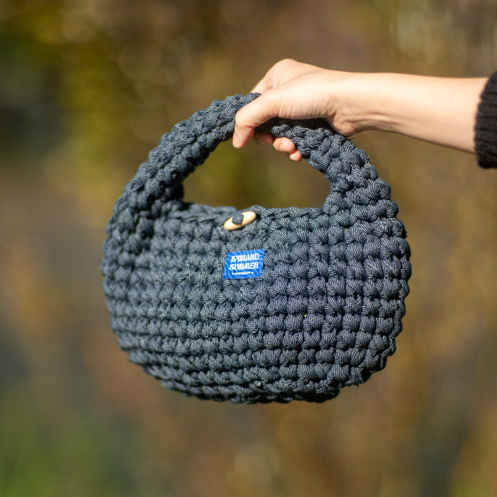 Hand holding a dark gray knitted handbag with a blurred natural background