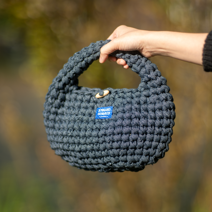 Hand holding a dark gray knitted handbag with a blurred natural background