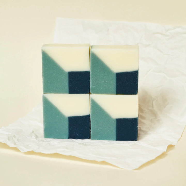 Four blue organic Ciment soaps stacked together, forming a new pattern, and placed on white paper.