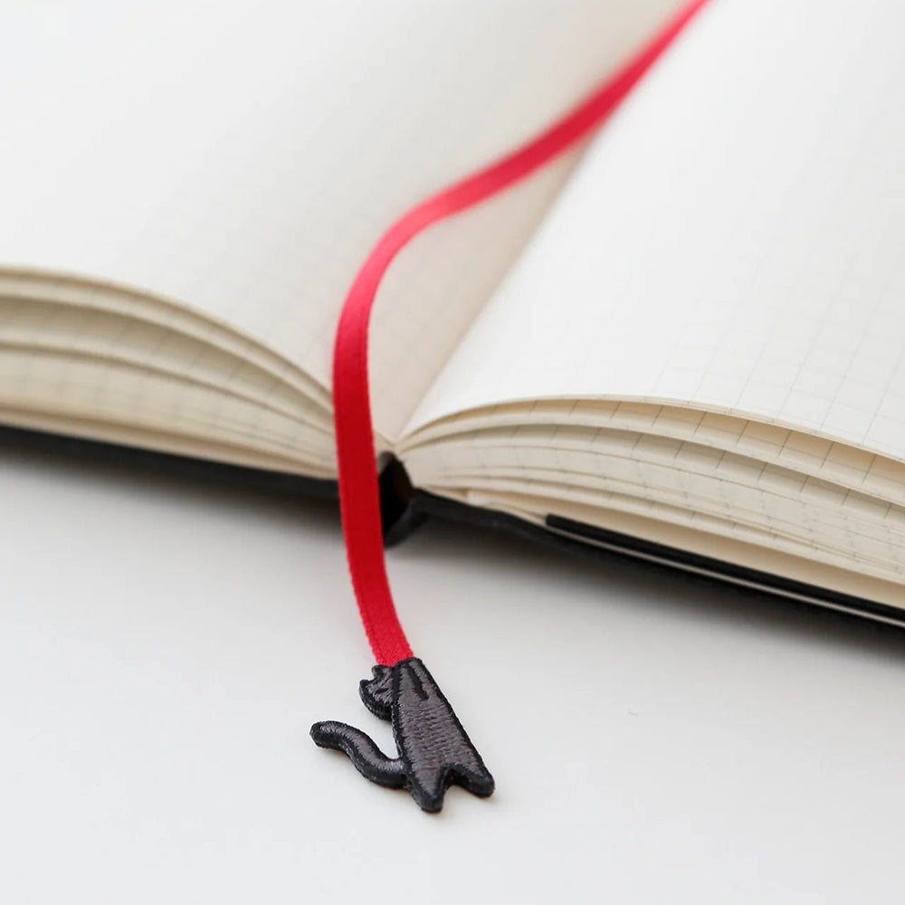 Black cat-shaped bookmark on a red string over an open book