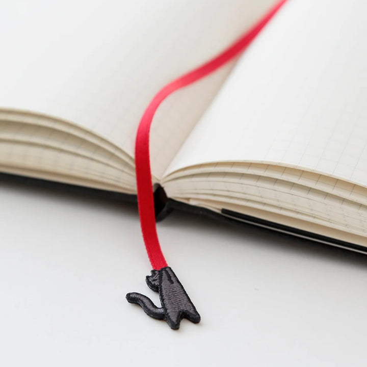Black cat-shaped bookmark on a red string over an open book