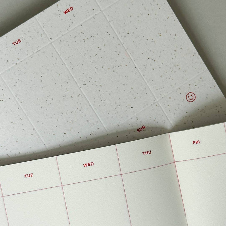 Close up of a Weekly Planner's cover and inner pages on a light gray background