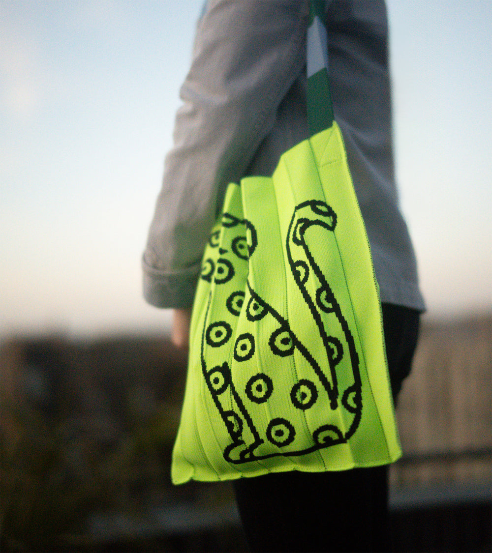 A model wearing a KNT 365 knitty tote bag in the Craig & Karl Neon Yellow style over her shoulder, adding a vibrant pop to her outfit.