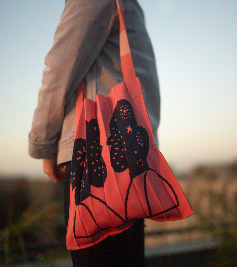 A model wearing a KNT 365 knitty tote bag in the Craig & Karl Pink style over her shoulder, complementing her outfit.