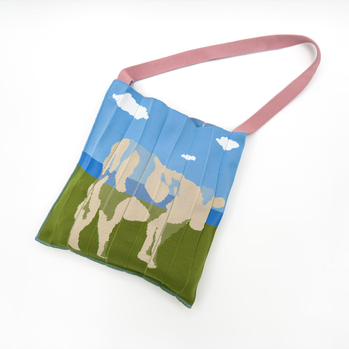 Image of the KNT 365 Knitty Tote Bag in beige, featuring a cow illustration, placed against a nature background, complemented by a pink strap, handmade in Japan to highlight its unique design and craftsmanship.