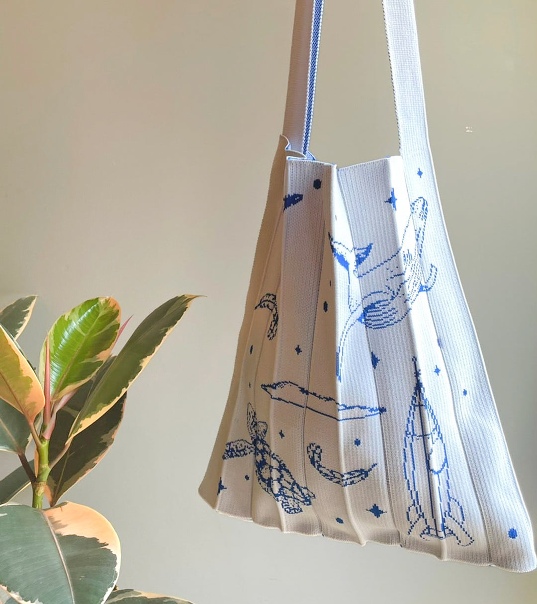 A white KNT 365 Knitty Tote Bag featuring space, planet, and animal illustrations, made in Japan, hanging against a wall to display its design and craftsmanship.