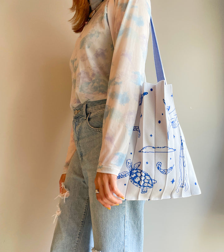 A model wearing the white KNT 365 Knitty Tote Bag with space, planet, and animal illustrations over her shoulder, paired with a casual daily outfit for a relaxed, stylish look.