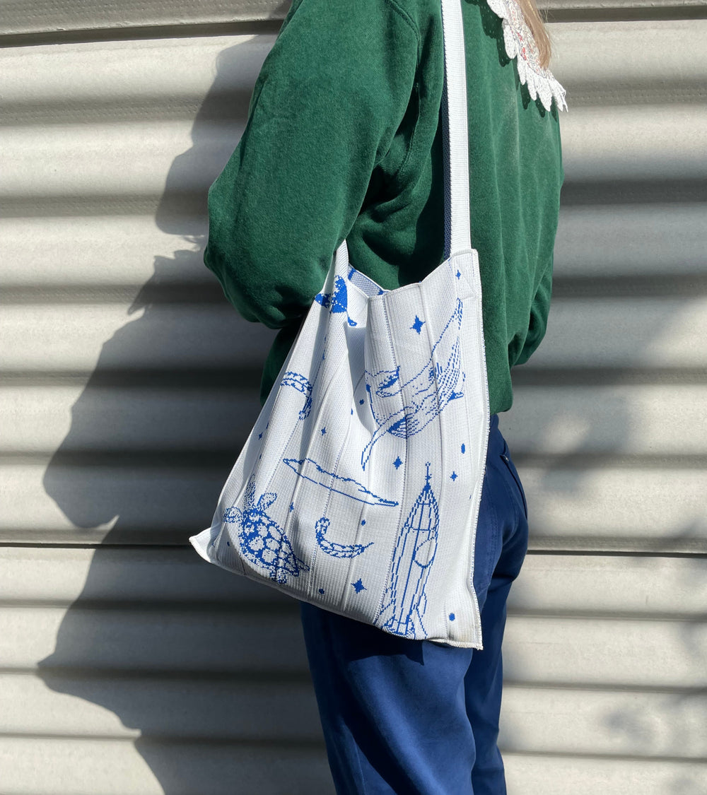 A model wearing the white KNT 365 Knitty Tote Bag with space, planet, and animal illustrations over her shoulder, paired with a green sweater, making the bag's design stand out beautifully.