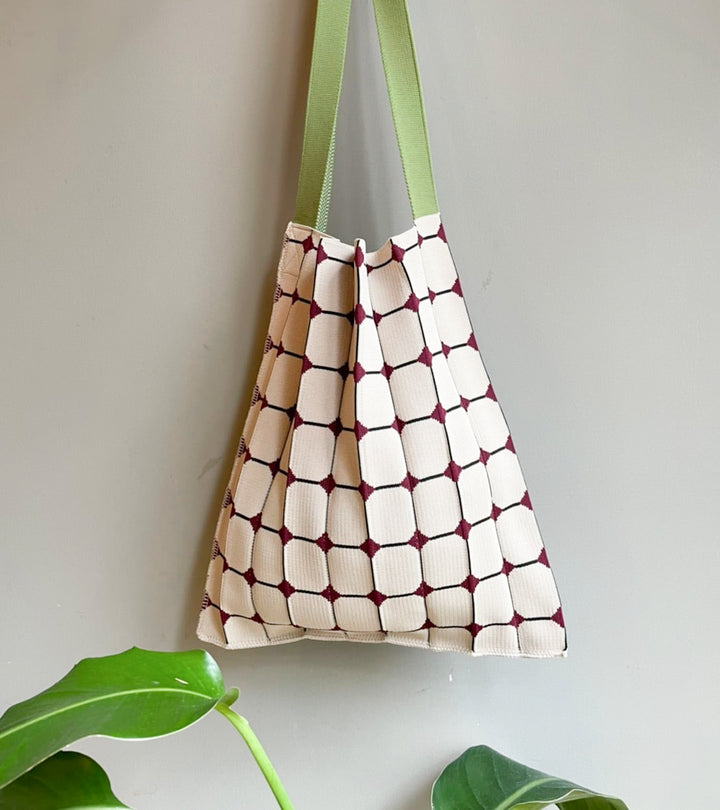 Image of the KNT 365 Knitty Tote Bag in beige with a diamond pattern and green straps, placed against a wall to highlight its handmade design and craftsmanship.