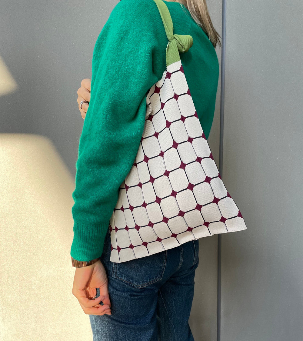 A model wearing the beige KNT 365 Knitty Tote Bag with a diamond pattern and green straps over her shoulder, paired with a green sweater, with the bag's strap shortened for a stylish fit.