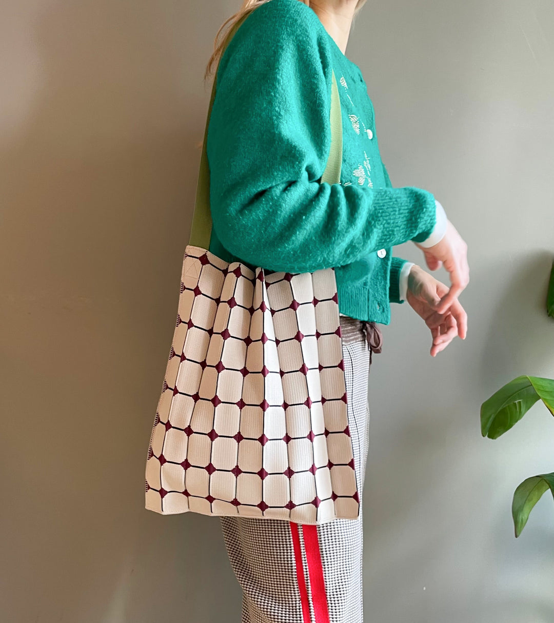 A model wearing the beige KNT 365 Knitty Tote Bag with a diamond pattern and green straps over her shoulder, paired with sporty trousers for an active and casual style.