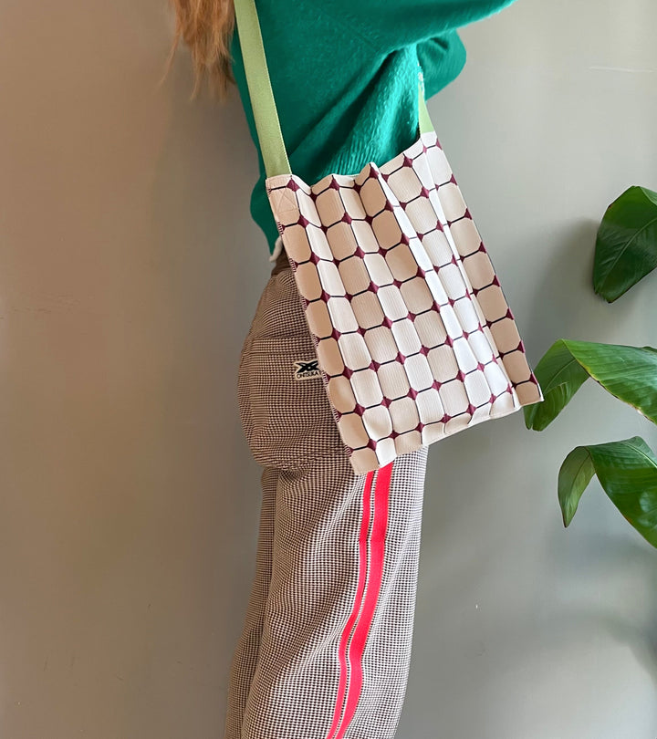 A model wearing the beige KNT 365 Knitty Tote Bag with a diamond pattern and green straps over her shoulder, paired with sporty trousers for an active and casual style.