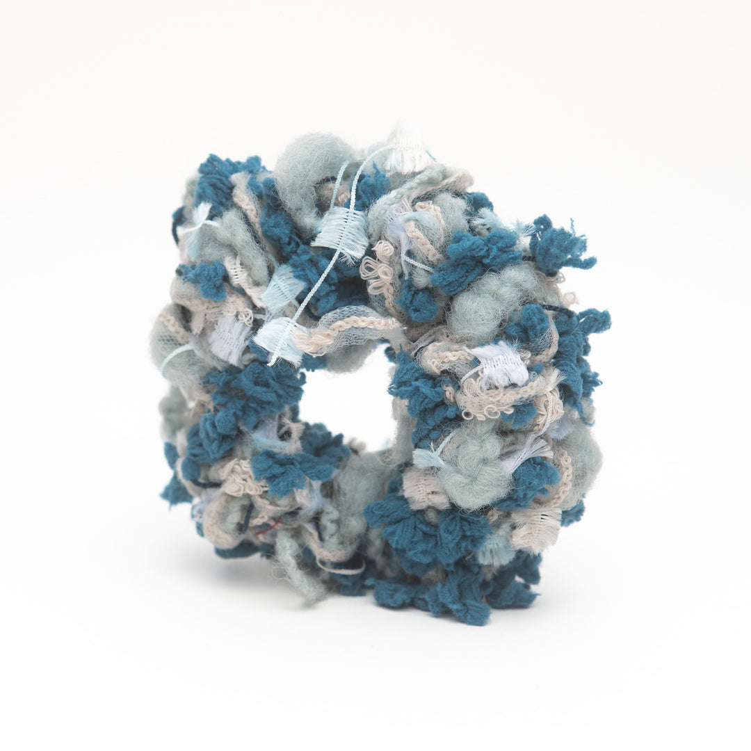 A handmade blue crochet scrunchie made from fluffy yarn, styled as a vibrant hair accessory.