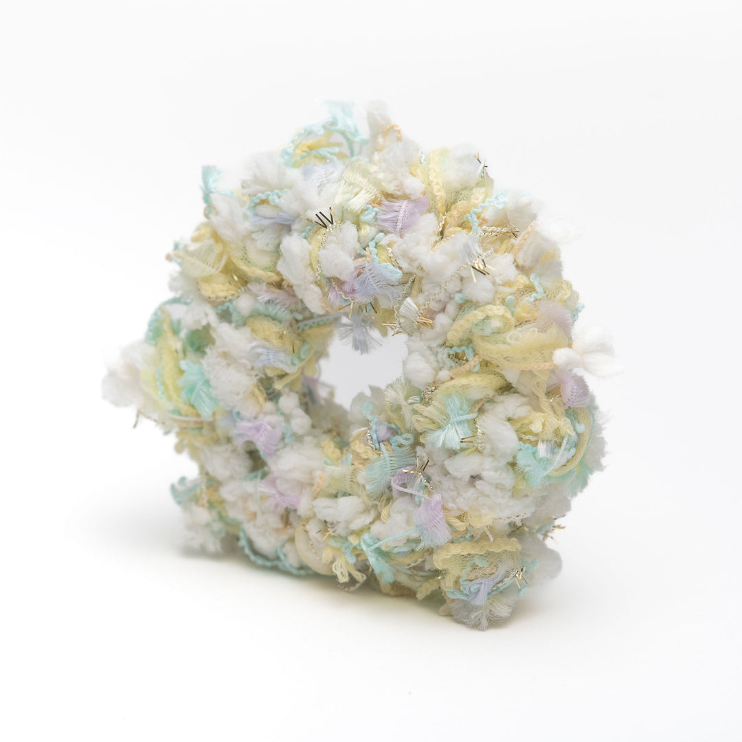 A handmade white crochet scrunchie with fluffy threads resembling cotton candy, styled as a vibrant hair accessory.